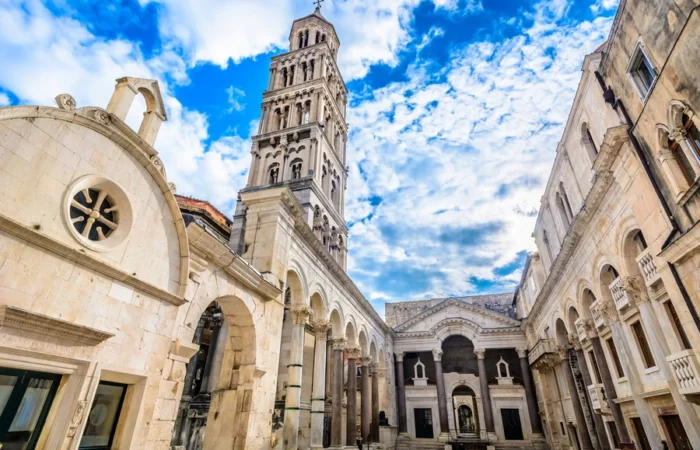 Diocletian’s Palace Peristyle square with Roman arches, columns, and the bell tower of St Domnius Cathedral under a blue sky, Split, Croatia.