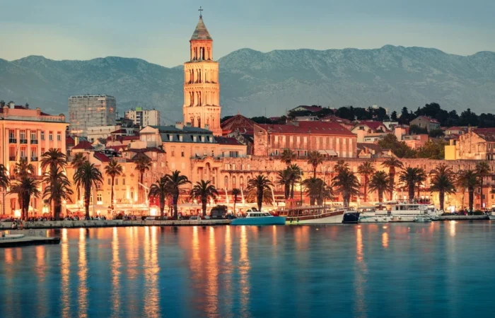 The lively Riva promenade with palm trees, Diocletian’s Palace, and the bell tower of St Domnius Cathedral in Split, Croatia, framed by sunset-lit mountains.