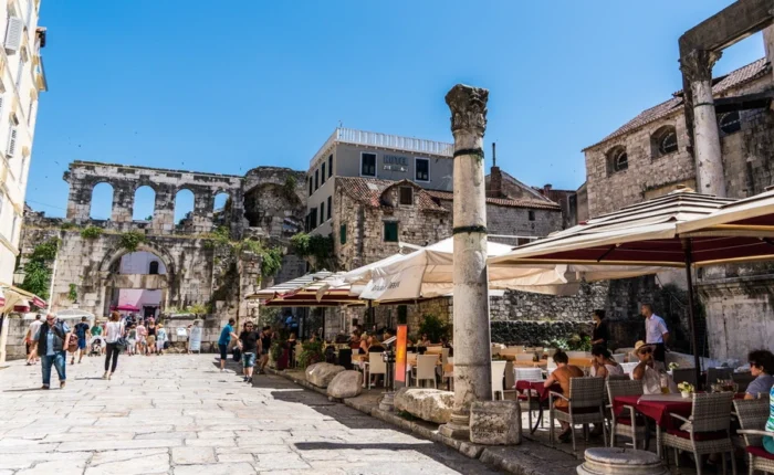 Outdoor café tables sit among ancient Roman columns and ruins by Split’s Silver Gate in Diocletian’s Palace, Croatia, on a sunny day.