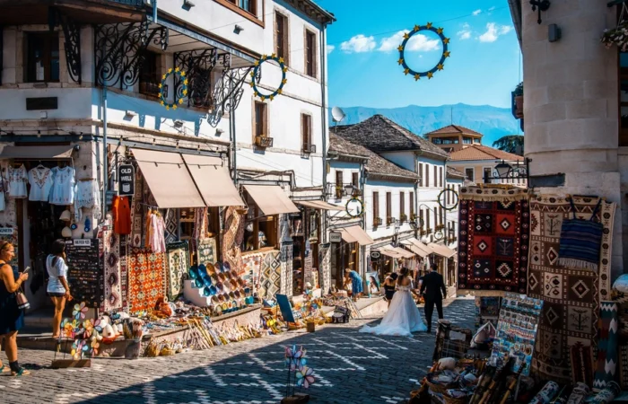 Colorful street scene at Tirana’s Pazari i Ri, with souvenir shops, textiles, white Ottoman-style buildings, and festive decorations under a clear sky.