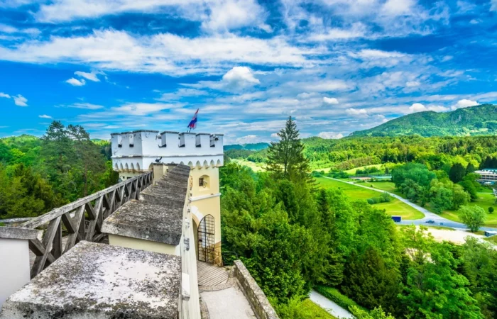 Wide-angle view of the neo-Gothic entrance and terrace at Trakošćan Castle, with turrets and decorative battlements against rural hills of northern Croatia.