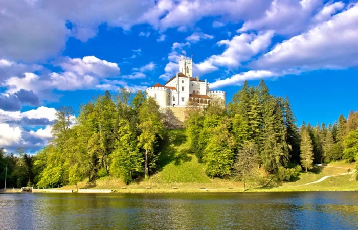 Trakošćan Castle sits on a hill surrounded by forests and reflected in a tranquil lake, with a dramatic sky and colorful foliage in northern Croatia.