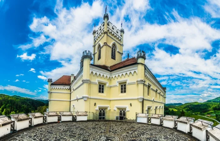 Bright view from the fortress ramparts and entrance of Trakošćan Castle, with its white tower, flag, and lush Zagorje landscape in Croatia.