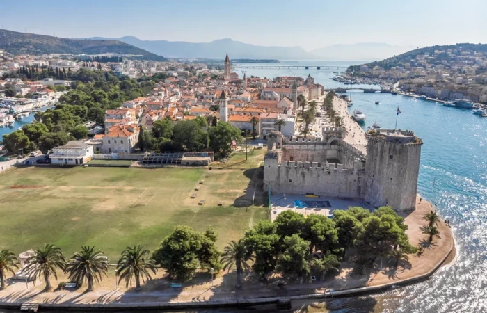 Kamerlengo fortress stands guard at the edge of Trogir, Croatia, with medieval townhouses, a palm-fringed promenade, and sunny harbor.
