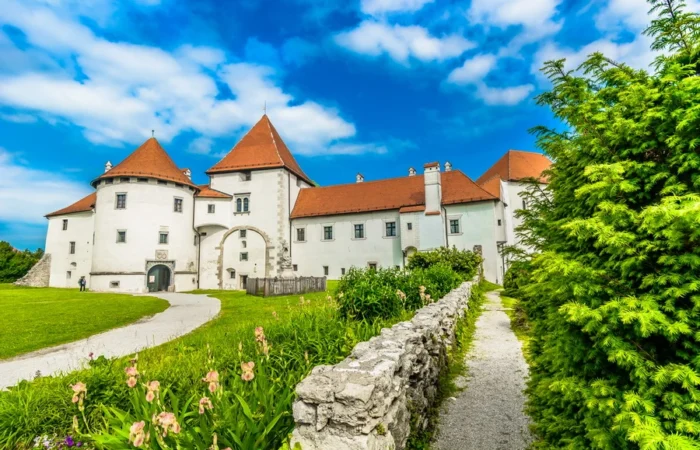 Varaždin’s Stari Grad castle, with white walls and red roofs, surrounded by lush gardens, spring flowers, and a stone path under a bright sky in northern Croatia.