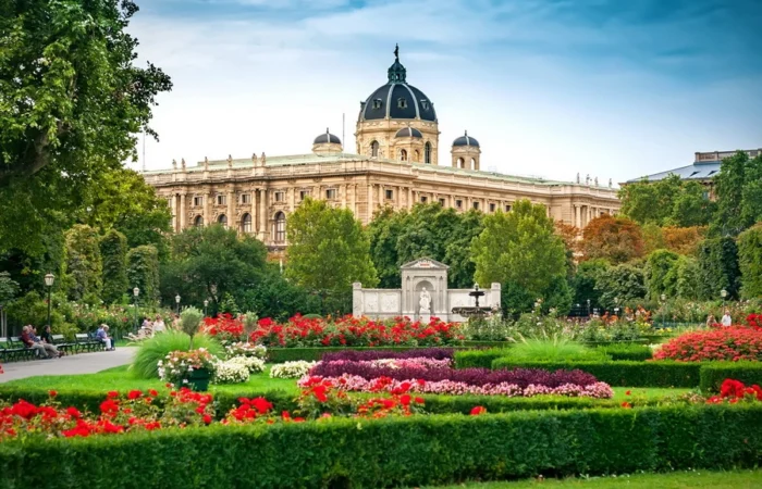 Rose gardens full of vibrant flowers in Vienna’s Volksgarten, with sculpted hedges and the grand Kunsthistorisches Museum dome in the background.
