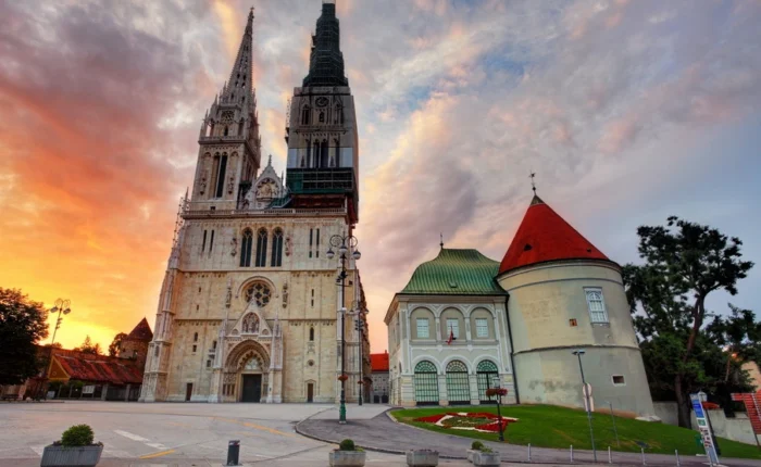 Zagreb Cathedral’s soaring neo-Gothic towers and baroque Kaptol fortifications set against a colorful sunset sky in Croatia’s capital city.