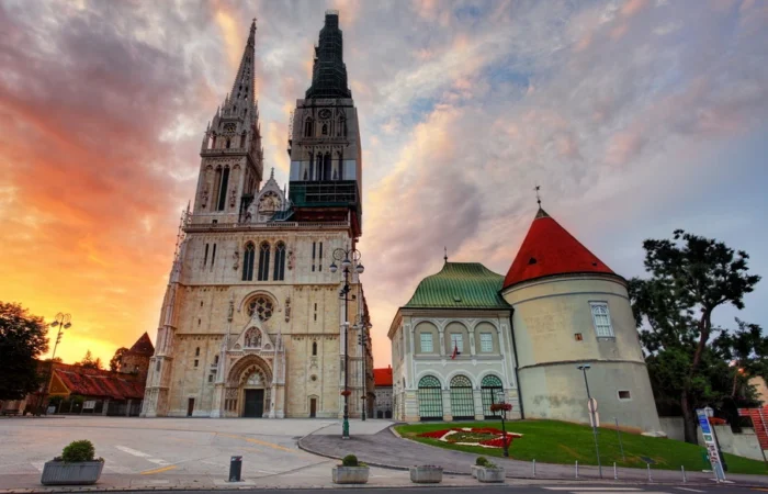 Zagreb Cathedral’s soaring neo-Gothic towers and baroque Kaptol fortifications set against a colorful sunset sky in Croatia’s capital city.