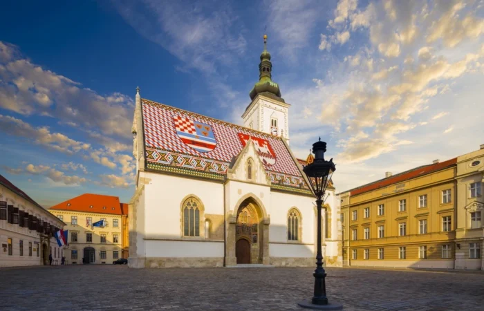 St. Mark’s Church in Zagreb’s Upper Town, Croatia, with its famous colorful tiled roof displaying the city and country coats of arms against a dramatic evening sky.