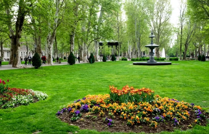 Lush green lawns, vibrant flower beds, tall trees, a central fountain, and gazebos in Zrinjevac park, Zagreb, Croatia - a tranquil urban oasis in springtime.
