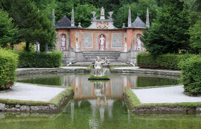 Baroque statues and ornate stone backdrop reflected in a tranquil pond at the trick fountains of Hellbrunn Palace in Salzburg, Austria.