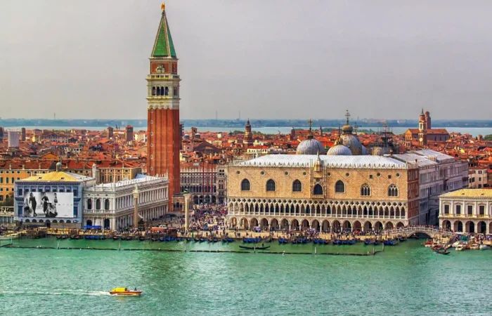 Panoramic view of Venice’s St. Mark’s Square waterfront with the Campanile bell tower and Doge’s Palace beside the turquoise lagoon.
