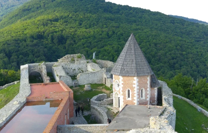 Stone walls and the conical-roofed chapel of Medvedgrad Fortress on Medvednica Mountain, surrounded by dense green forest above Zagreb.