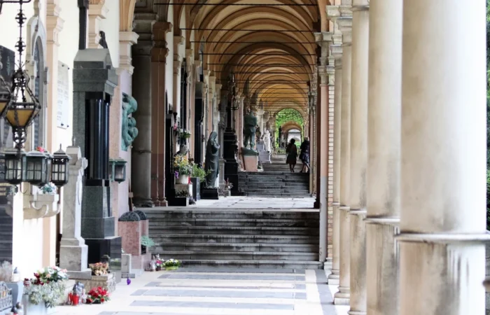 Long arched arcade at Mirogoj Cemetery in Zagreb with stone columns, tombs, statues and flower arrangements along the corridor.